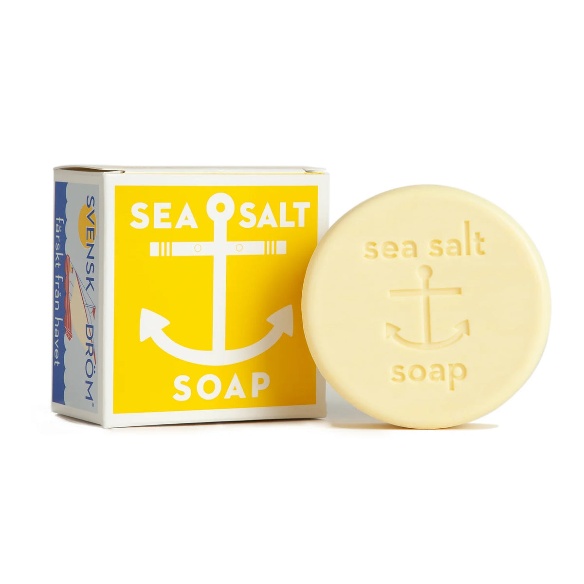 A bar of Swedish Dream Sea Salt Lemon Soap with a round shape, embossed with the words "sea salt" and an anchor symbol. Infused with lemon citrus oils, the light beige soap is positioned next to its packaging, which is predominantly yellow with white text and an anchor design.