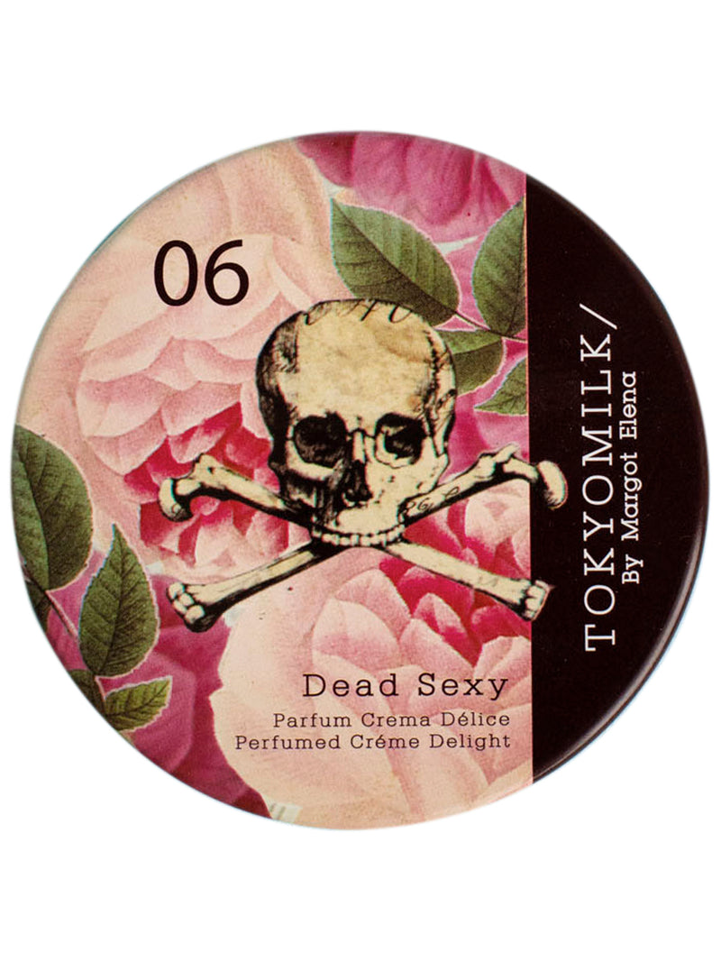 A round label for Margot Elena's TokyoMilk Dead Sexy Parfum Crema with a design featuring a skull and crossbones over a background of pink and red floral patterns. The label has text and