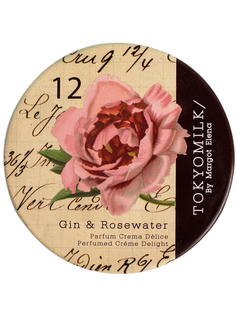 A round cosmetic lid featuring a vintage-style design with a blooming pink rose, scripted handwriting, and a dark brown section with the text "Margot Elena TokyoMilk Gin & Rosewater Parfum Crema Délice.