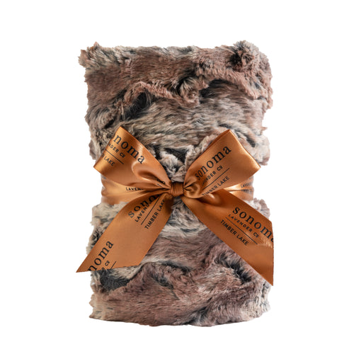 A plush, gray and brown faux fur Sonoma Lavender Timber Lake Warm Chestnut Heat Wrap neatly rolled up and secured with an elegant terracotta ribbon that reads "Sonoma" in white lettering, isolated on a white background.