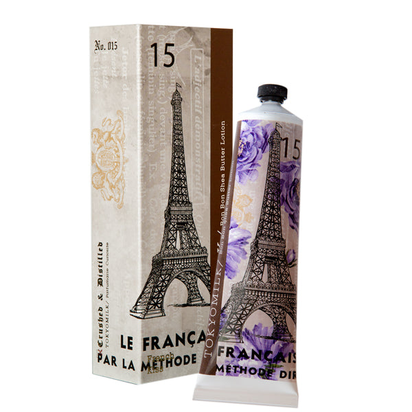 Tube of TokyoMilk French Kiss No. 15 Bon Bon Shea Butter Lotion with an Eiffel Tower design beside its packaging showing similar artwork with floral accents and mimosa bark, indicating a French theme by Margot Elena.