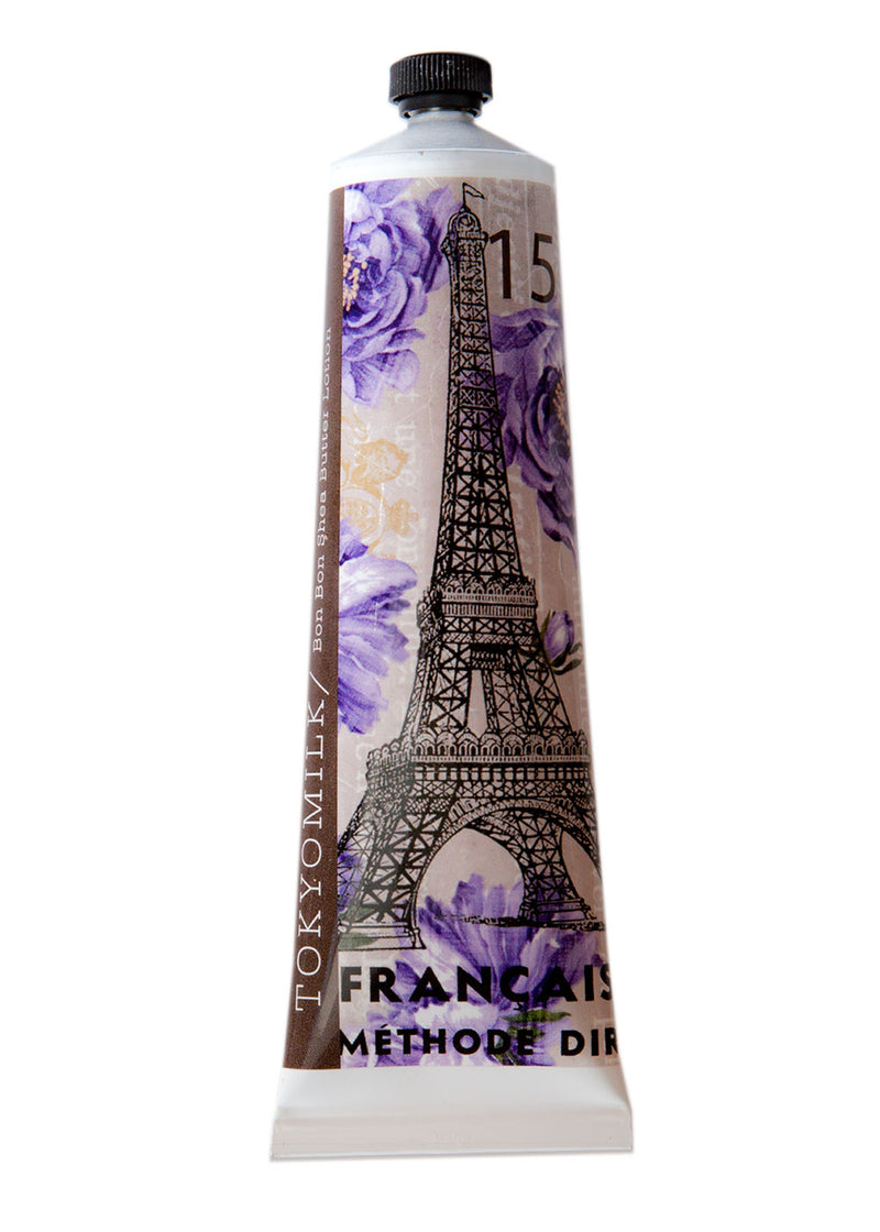 A tube labeled "Margot Elena's TokyoMilk French Kiss No. 15 Bon Bon Shea Butter Lotion" featuring artistic designs with an Eiffel Tower graphic and floral patterns in shades of purple and white, infused with mimosa bark.