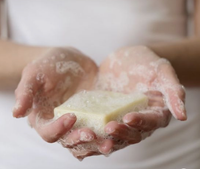 A person holding a soapy sponge in their hands, with soap suds visible around the hands and sponge, emphasizing hygiene or cleaning with Hydra Bloom Beauty Relax Lavender Organic Soap from Hydra Bloom Beauty Lavender.