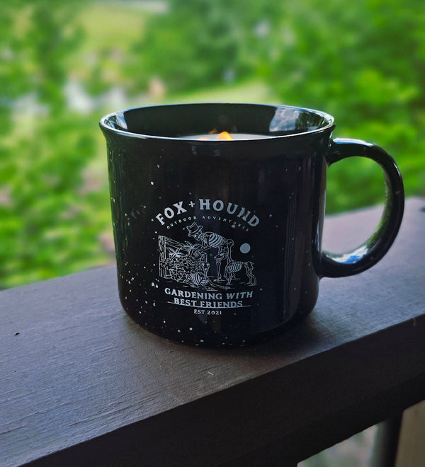 The Fox + Hound Ginger & Saffron Citronella Soy Candle comes in a black speckled ceramic gardening mug, blending insect-repelling citronella with a charming fox and dog illustration—perfect for enjoying the outdoors.