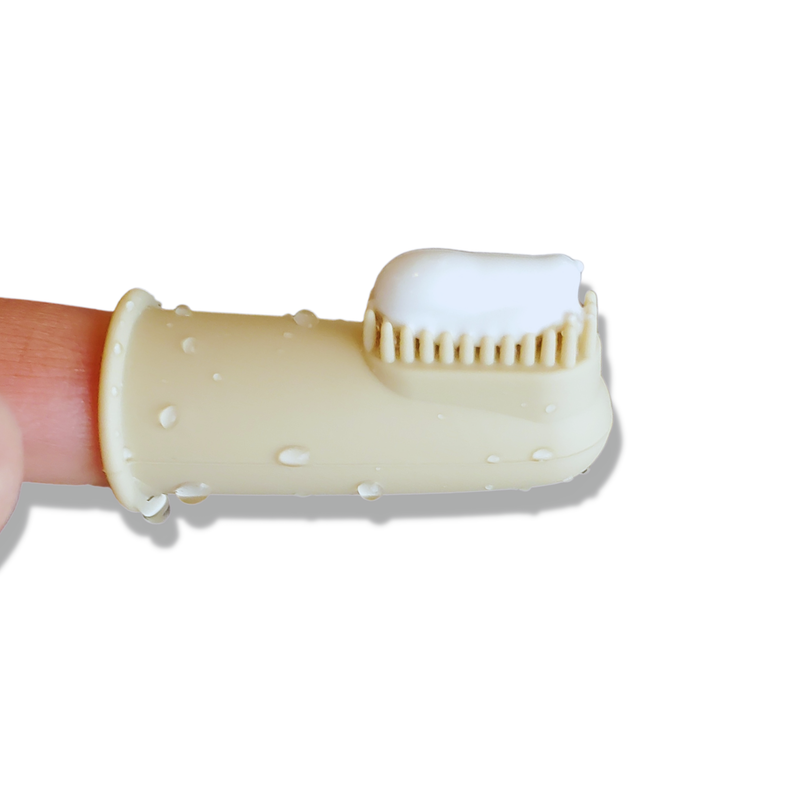 The Puppy Polisher Finger Brush from Wag & Bright Supply Co. is displayed on a finger against a white background. This beige finger brush, suitable for infants or pets, includes silicone bristles with water droplets shimmering on its surface.