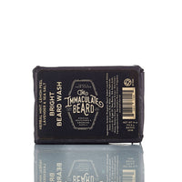 The Immaculate Beard SUNRISE Beard Wash Bar, a black 4 oz charcoal shampoo bar, features herbal mint, lemon peel, lavender, and sea salt for premium beard care. Its packaging is reflected on a white surface.