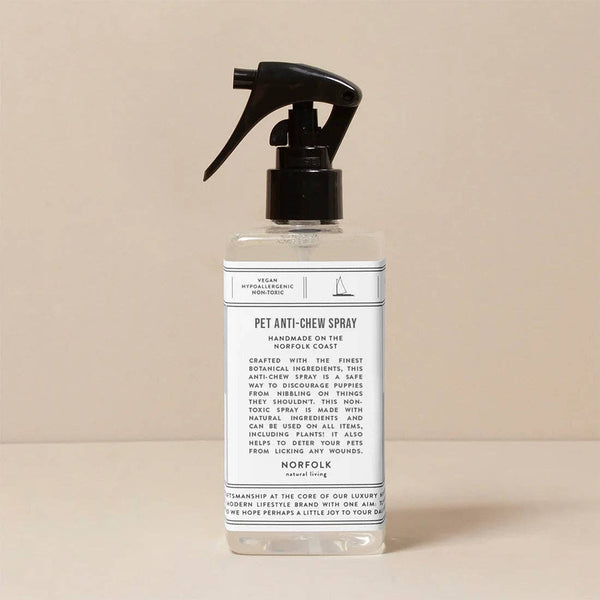 A clear spray bottle of Norfolk Natural Living Pet Anti-Chew Spray with a black trigger nozzle rests on a neutral surface. Its label highlights a vegan, non-toxic formula with handmade botanicals for safe, effective pet care.