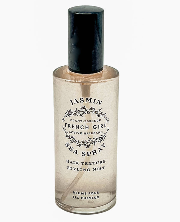 A clear bottle with a black cap labeled "FRENCH GIRL Organic Sea Salt Hair Mist & Texturizing Spray - Jasmine" creates effortless beachy waves and adds texture, featuring a botanical design for clean hair care.
