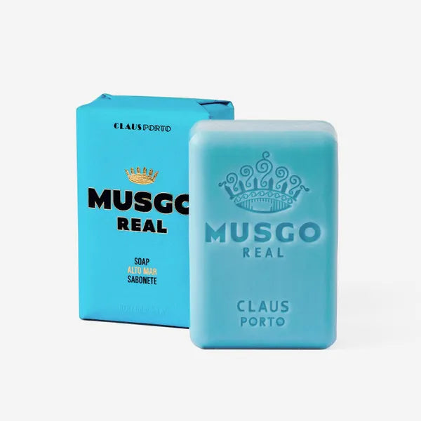 A blue bar of Claus Porto 1887's Musgo Real Alto Mar Body Soap enriched with bladderwrack extract next to its matching blue and teal packaging, displayed against a plain white background.