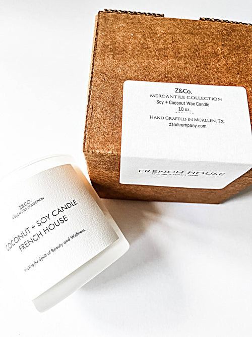 A Z&Co. French House Mercantile Candle, featuring premium soy and coconut wax in a white glass jar with a double wick, sits next to a matching labeled brown box. This handcrafted item from McAllen, TX is part of the Z&Co. Mercantile Collection.