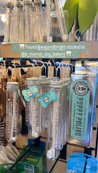 A display featuring dog dental care products, including tubes and boxes labeled "Puppy Polish," along with the innovative Wag & Bright Supply Co. - Puppy Polisher Eco Toothbrush (Medium), is showcased at a store. The text overlay highlights that these pet dental health essentials are available at select retailers.