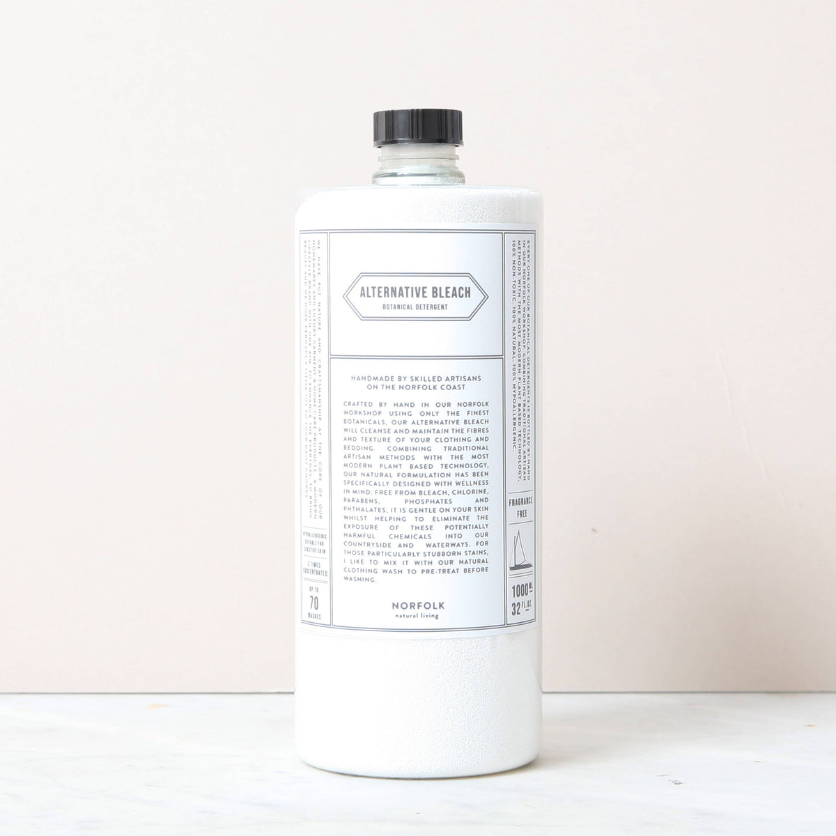 A white bottle of Norfolk Natural Living Alternative Bleach, an eco-friendly disinfectant with a black cap and minimalist label, stands upright on a light surface against a pale background, reflecting its non-toxic cleaner formula.