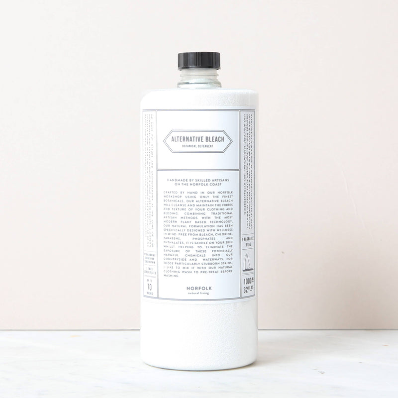 A white bottle of Norfolk Natural Living Alternative Bleach, an eco-friendly disinfectant with a black cap and minimalist label, stands upright on a light surface against a pale background, reflecting its non-toxic cleaner formula.