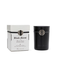 The Archipelago Botanicals Black Forest Boxed Candle, in a sleek black holder with silver accents and medallion, sits beside its elegant white box—perfect for any scented candle lover.
