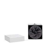 A white square gift box with its lid off reveals a black spiral, evoking the elegance of luxury candles like the Archipelago Black Forest Boxed Candle by Archipelago Botanicals, against a plain white background.