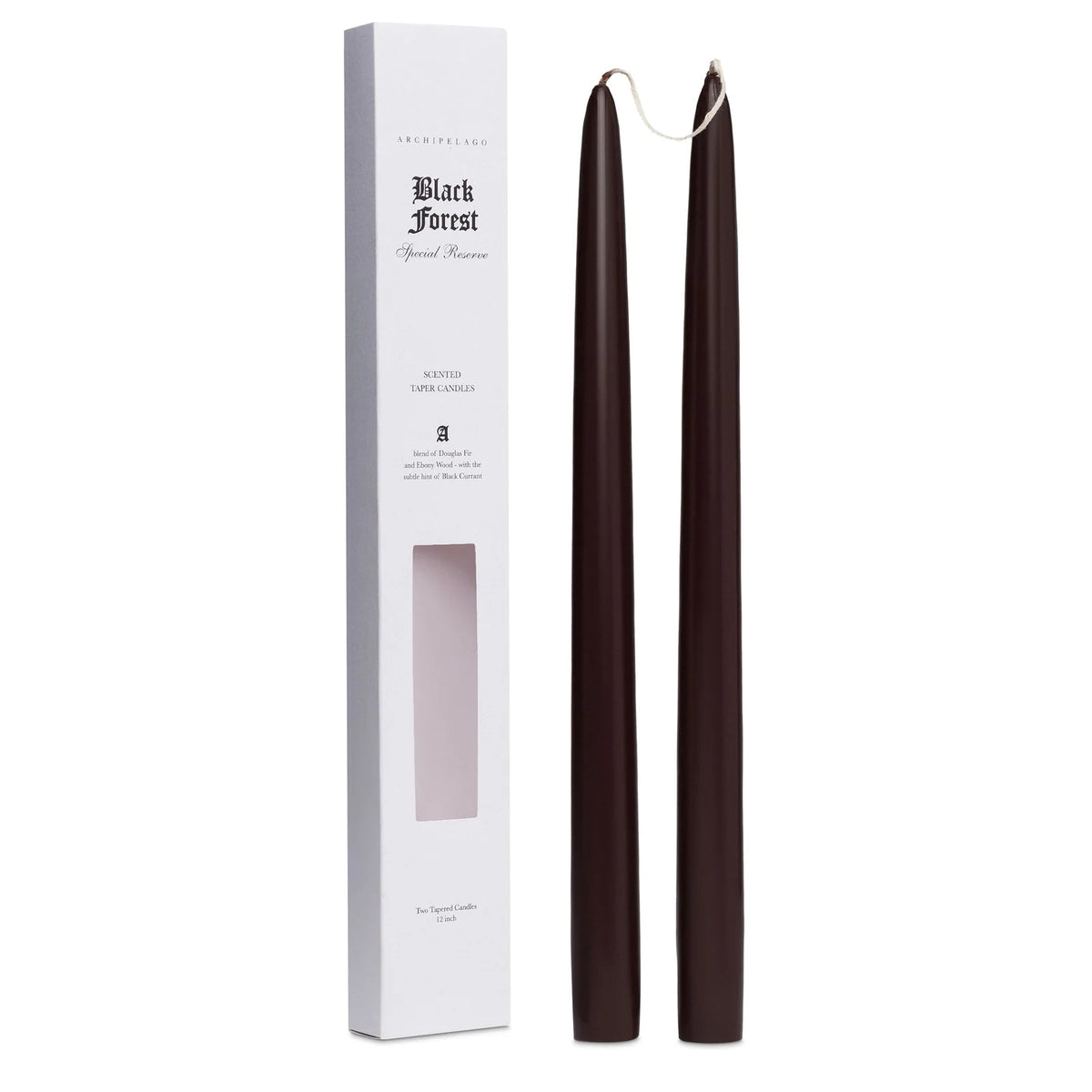 Two tall, dark brown Archipelago Black Forest Tapered Candles by Archipelago Botanicals stand upright next to a white rectangular box labeled “Black Forest Special Reserve,” which features a window displaying the scented candles inside.