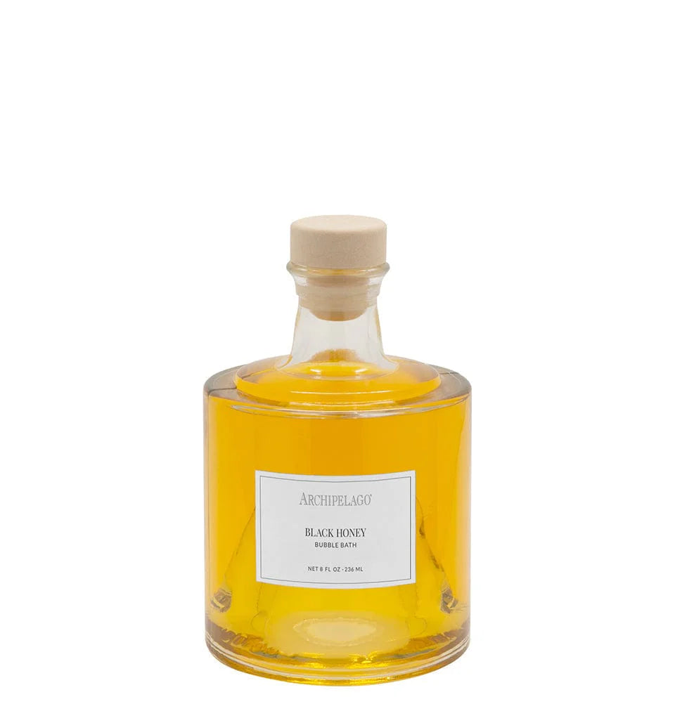 A clear glass bottle filled with yellow liquid, sealed with a beige cap, and labeled "Archipelago Botanicals Black Honey Bubble Bath" offers skin-softening ingredients and a luxurious bath experience from Archipelago Botanicals.