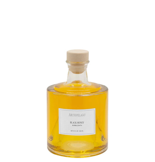 A clear glass bottle filled with yellow liquid, sealed with a beige cap, and labeled "Archipelago Botanicals Black Honey Bubble Bath" offers skin-softening ingredients and a luxurious bath experience from Archipelago Botanicals.
