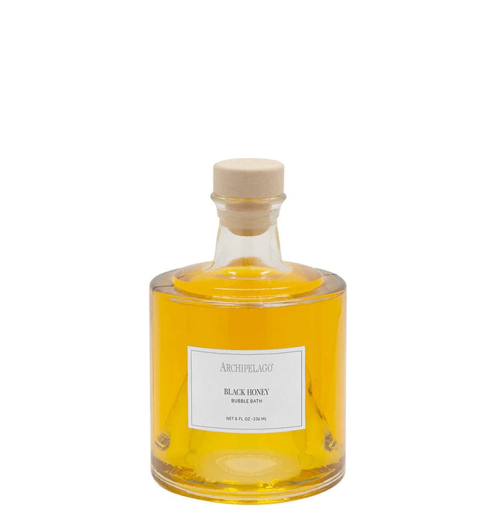 A clear glass bottle filled with yellow liquid, sealed with a beige cap, and labeled "Archipelago Botanicals Black Honey Bubble Bath" offers skin-softening ingredients and a luxurious bath experience from Archipelago Botanicals.