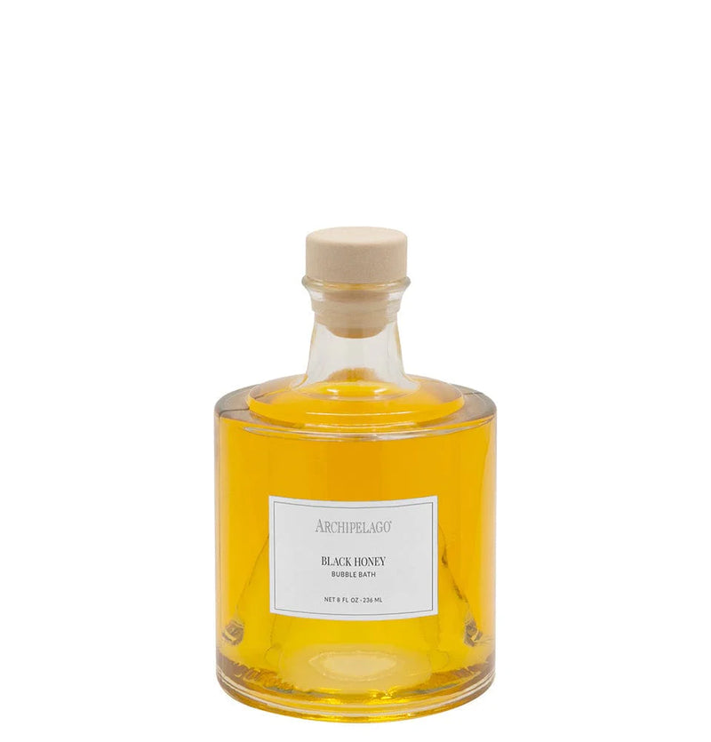A clear glass bottle filled with yellow liquid, sealed with a beige cap, and labeled "Archipelago Botanicals Black Honey Bubble Bath" offers skin-softening ingredients and a luxurious bath experience from Archipelago Botanicals.
