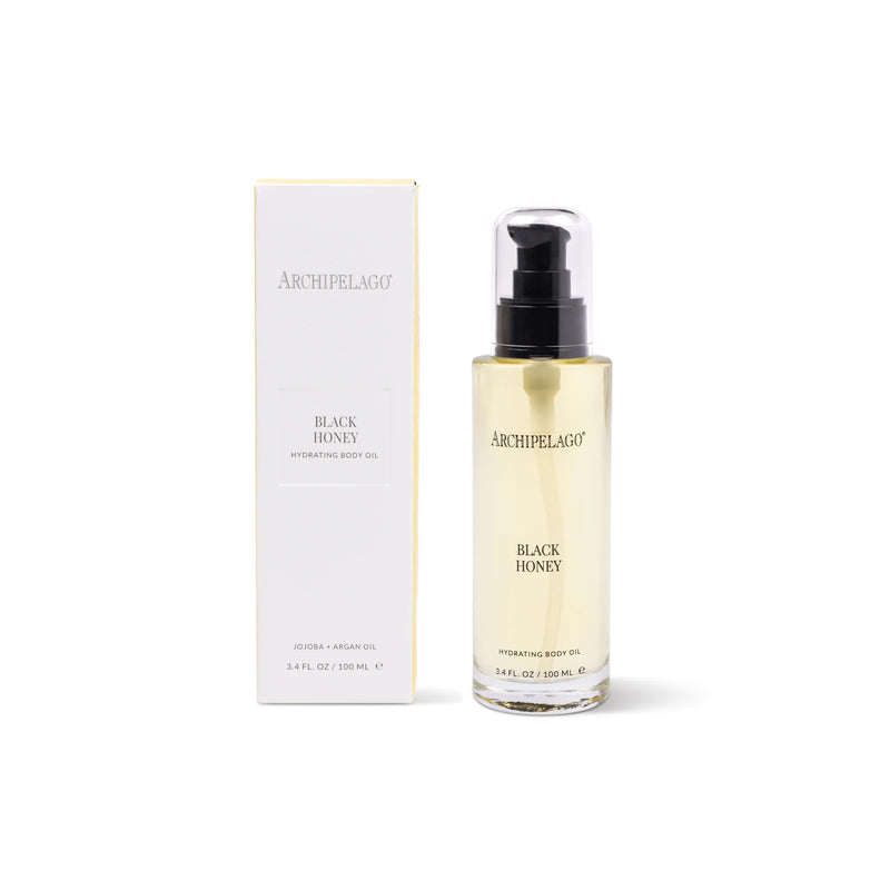 A bottle of Archipelago Botanicals Black Honey Hydrating Body Oil with a black pump is shown next to its white and gold box, both labeled with the product name—perfect for hydrating dry skin and supporting skin regeneration.