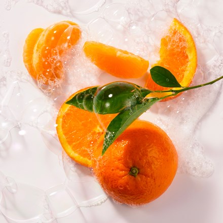 Whole oranges with green leaves and slices on a white surface, adorned with soap bubbles, evoke the refreshing scent of Roger & Gallet Orange Wood Wellbeing Soaps Set 3 x 3.5 oz by Roger & Gallet.