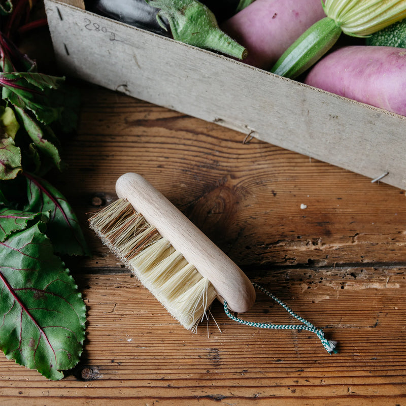 An Andrée Jardin Hard and Soft Fibres Vegetable Brush from Andrée Jardin sits on a rustic wooden table beside fresh produce. Leafy greens and an assortment of nutrient-rich vegetables are neatly arranged in a wooden crate.