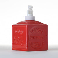 A red, square-shaped ceramic soap dispenser with a pump top, branded as FRENCH SOAPS' French Soaps Liquid Soap Dispenser Savon de Marseille. The bottle features raised text that reads "Savon Superieur Marseille" on the front, along with a decorative floral design. Its traditional charm is enhanced by the plain white background, making this Savon de Marseille dispenser the focal point.