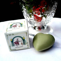 A Senteurs De France Olive Heart Soap - Marquise and Her Dog, a decorative glass, and a small illustrated “Senteurs De France” box are displayed on a white surface, celebrating French heritage.