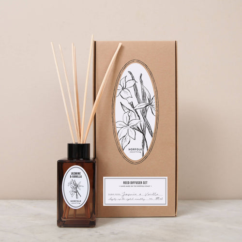 The Norfolk Natural Living Jasmine & Vanilla Reed Diffuser Set features a brown glass bottle with wooden sticks and a botanical-illustrated box—ideal for bringing natural fragrance to your home.
