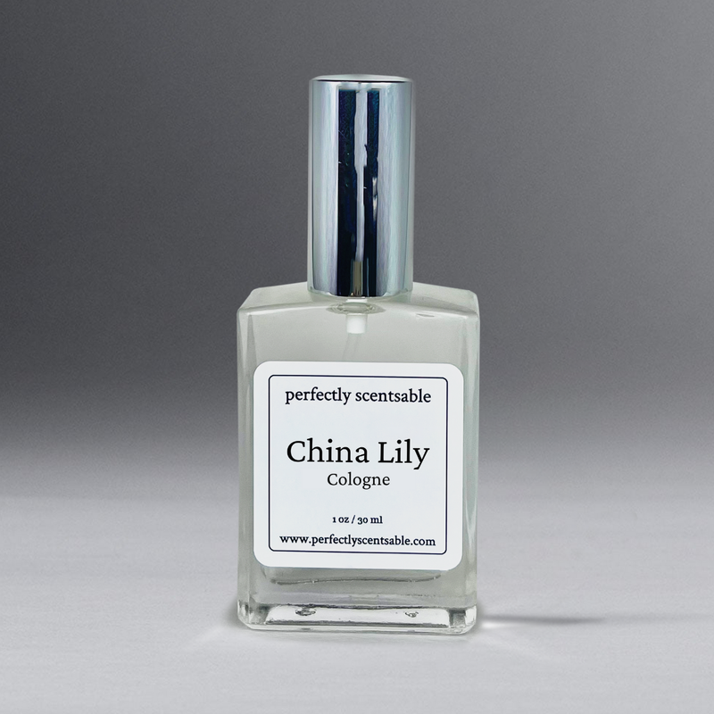 A 1 oz. cologne spray bottle of "Perfectly Scentsable China Lily Perfume Oil" is shown against a gradient gray background. The bottle features a silver cap, and the label reads "Perfectly Scentsable China Lily Perfume Oil" with a website URL, "www.perfectlyscentsable.com", at the bottom.