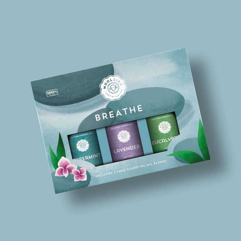 The Woolzies The Breathe Essential Oil Collection features eucalyptus, peppermint, and lavender oils in blue-green packaging with floral and leaf illustrations for a charming look.