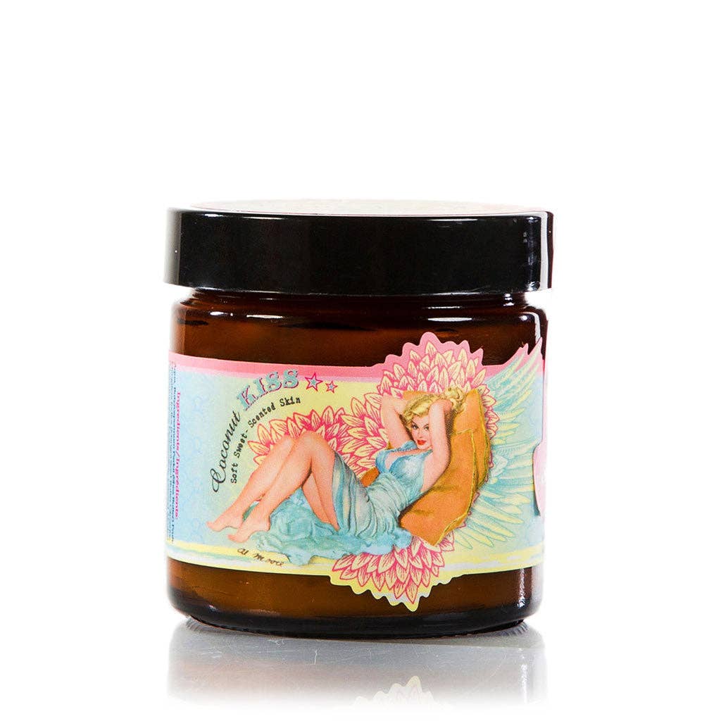 A brown glass jar with a black lid features a colorful label depicting a reclining woman in a blue dress surrounded by pink flowers. The label reads "Barefoot Venus Coconut Kiss Instant Hand Repair Balm" and other decorative elements, highlighting its nourishing blend of Shea Butter and Mango Seed Butter.