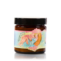 A brown glass jar with a black lid features a colorful label depicting a reclining woman in a blue dress surrounded by pink flowers. The label reads "Barefoot Venus Coconut Kiss Instant Hand Repair Balm" and other decorative elements, highlighting its nourishing blend of Shea Butter and Mango Seed Butter.