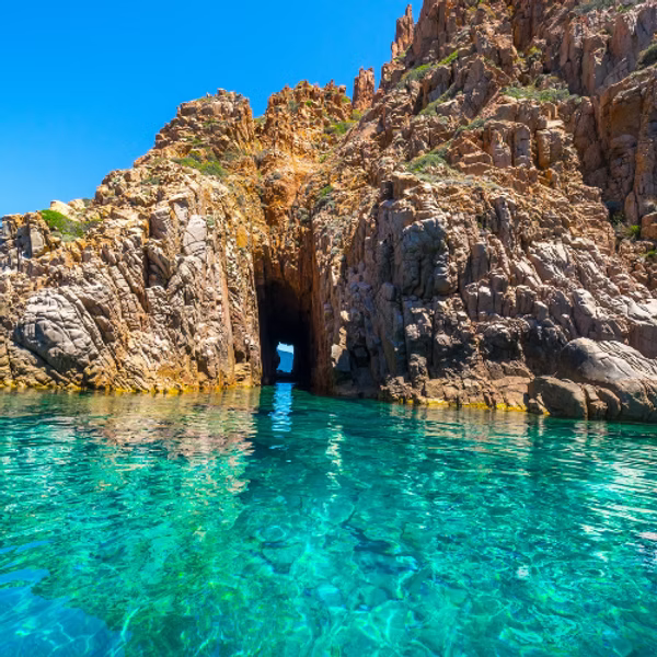 Clear turquoise water, rocky cliffs, and a natural archway under a sunny sky evoke the Mediterranean allure of ISULA parfums Calanque de Piana eau de toilette by ISULA parfums.