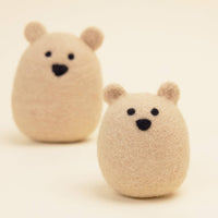Two small, round MODERNBEAST Wool Polar Bear Dog Toys by MODERNBEAST are shown on a plain light background, one in focus at the front and another slightly blurred behind.
