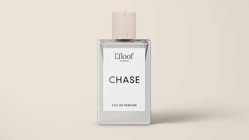 A bottle of dog perfume labeled "L'floof CHASE" from the brand "L'floof." This chypre fragrance comes in a rectangular bottle with a white and beige cap. The label, featuring a minimalist design in black text, rests gracefully against a neutral beige background.