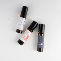 Three Nustad Family Ranch Essential Oil Perfume Roller Golden Hour bottles with stylish labels, including "driftwood" and "flight," arranged on a light grey background.