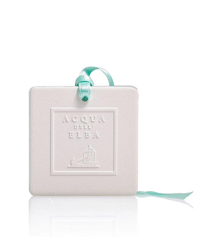 The Acqua dell'Elba Mare Scented Ceramic Air Freshener by Acqua dell'Elba features a white, square ceramic design embossed with the brand name, is infused with Isola d’Elba fragrance, and hangs from a light blue ribbon against a white background.
