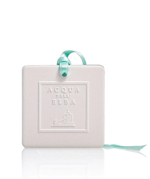 The Acqua dell'Elba Mare Scented Ceramic Air Freshener by Acqua dell'Elba features a white, square ceramic design embossed with the brand name, is infused with Isola d’Elba fragrance, and hangs from a light blue ribbon against a white background.