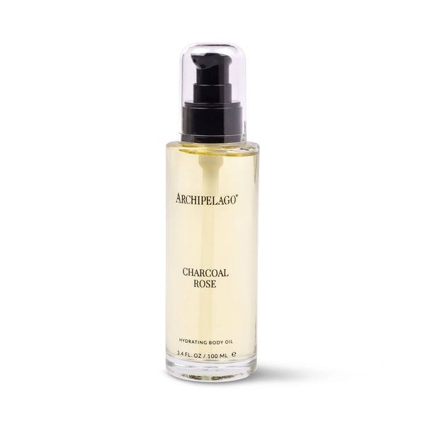 A clear bottle of Archipelago Botanicals Charcoal Rose Hydrating Body Oil with a black pump holds 3.4 fl oz / 100 mL of light yellow, nourishing oil—ideal for natural skincare routines. The label shows the product and brand name.