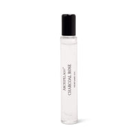 A clear glass rollerball bottle with a black cap, labeled "Archipelago Charcoal Rose Perfume Oil" by Archipelago Botanicals, stands upright against a white background. This long-lasting perfume features bold black text on the front.