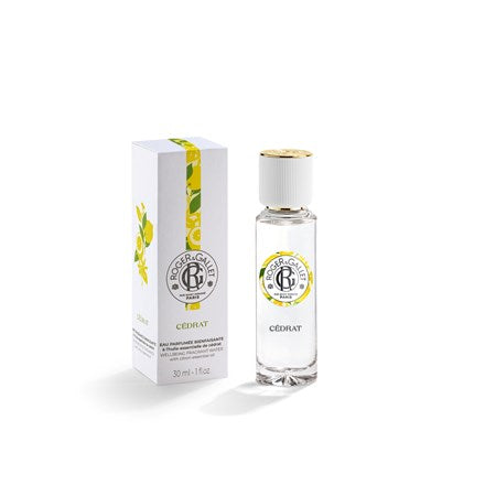 A clear glass bottle of Roger & Gallet Citron Wellbeing Fragrant Water 1 oz stands next to its matching white box, both decorated with lemon designs and gold accents, set against a plain white background.