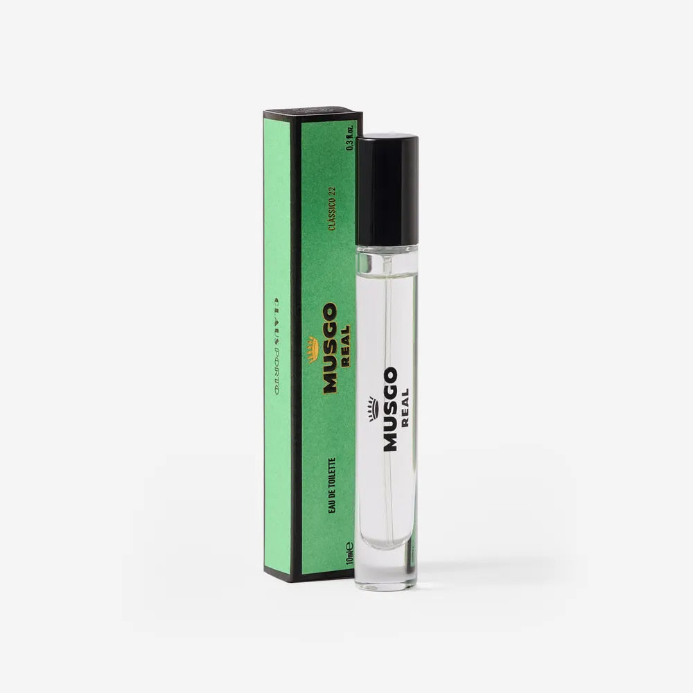 A clear glass bottle of Claus Porto Musgo Real Clássico 22 Eau de Toilette Travel Size by Claus Porto 1887 stands beside a tall, green, rectangular box with black accents and text, set against a white background.