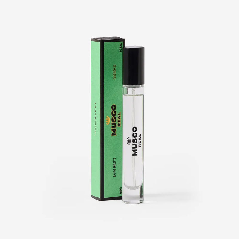 A clear glass bottle of Claus Porto Musgo Real Clássico 22 Eau de Toilette Travel Size by Claus Porto 1887 stands beside a tall, green, rectangular box with black accents and text, set against a white background.
