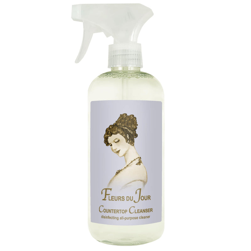 A spray bottle of "La Bouquetiere Fleurs du Jour Marina Blue" countertop cleanser with a vintage-style label featuring an illustration of a woman with an elegant updo hairstyle.