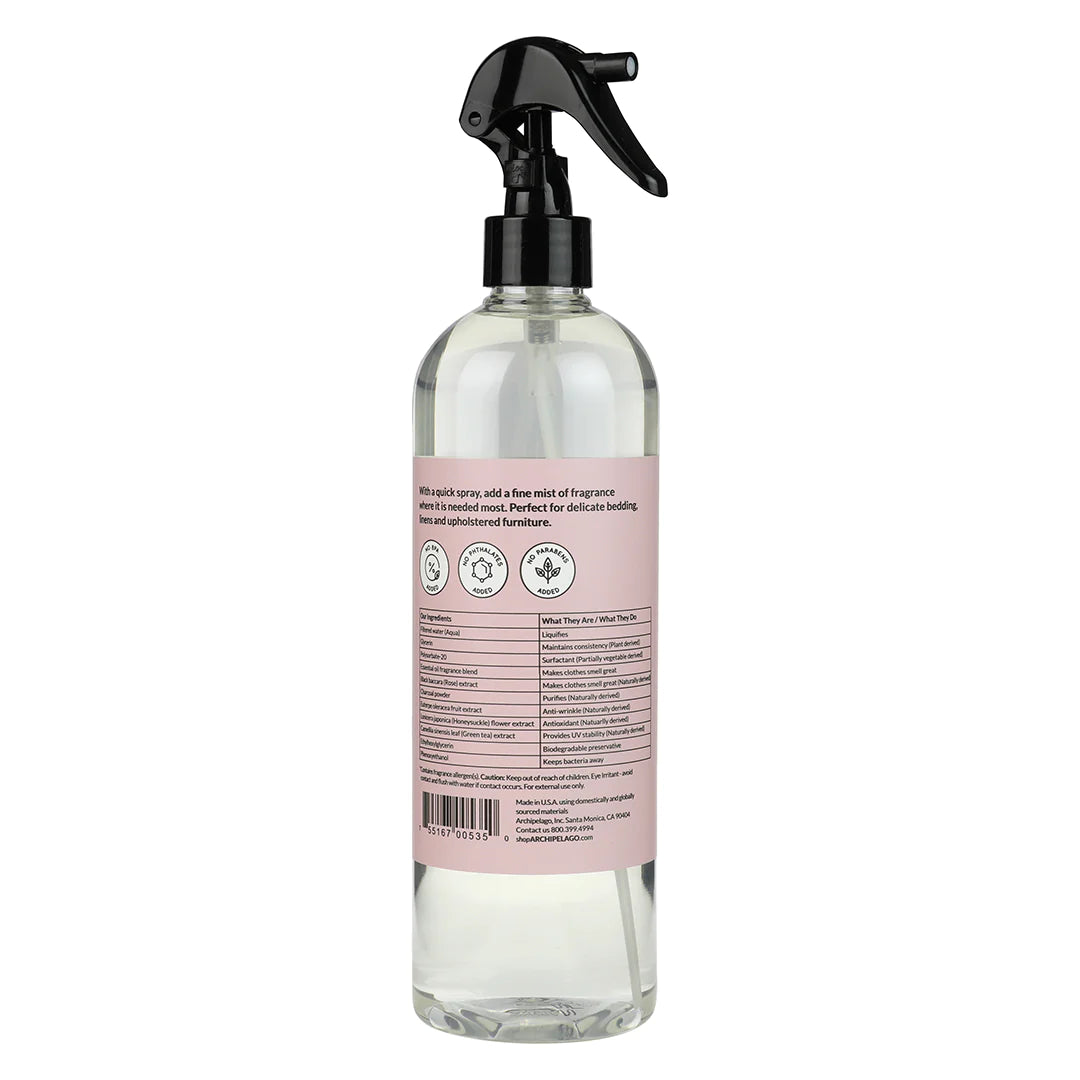 Clear spray bottle with a black trigger sprayer, showing the label with product details and instructions in black and pink text for Archipelago Charcoal Rose Linen Spray by Archipelago Botanicals. Safe disposal and recycling symbols are also present.