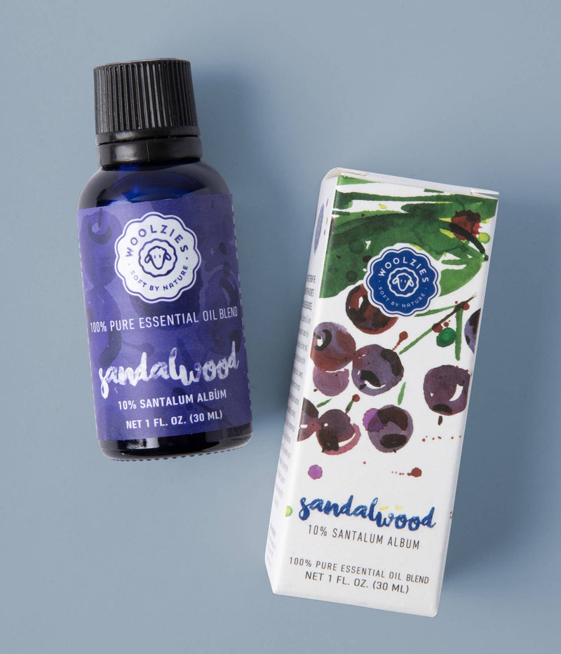 Woolzies Sandalwood Essential Oil comes in a dark bottle with a purple label and a white box featuring watercolor sandalwood berries, offering a soothing aroma ideal for relaxation and skin support.