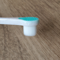 A close-up of the Wag & Bright Supply Co. Puppy Polisher Pearl Eco Toothbrush head showcases soft white bristles alongside a green rubber pad on top. The BPA-free handle, adorned with brown speckles, elegantly rests on a wooden surface, making it perfect for ensuring optimal dental health for your dog.