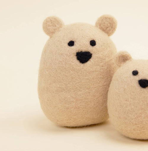 A close-up of two MODERNBEAST Wool Polar Bear Dog Toys, crafted from beige felt with stitched black eyes and noses, set against a light background. The full-size toy is visible while the smaller one appears partially on the right.